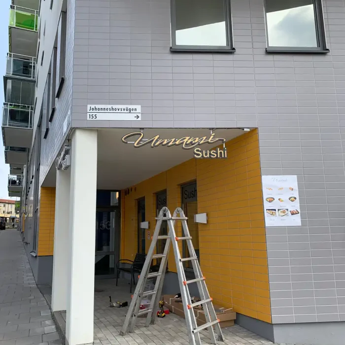 Fasadskylt hängande på ram i Årsta Stockholm för Umami Sushi.
