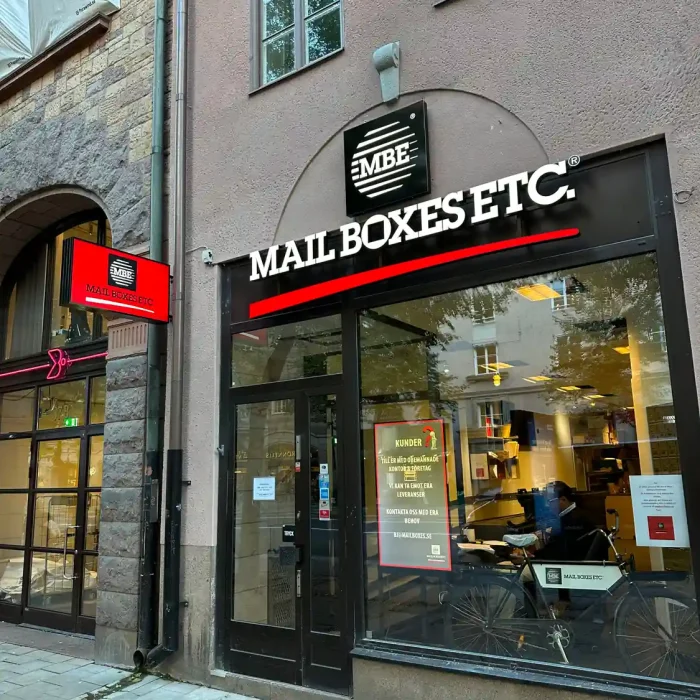Fasadskylt Stockholm för MBE mailboxes på Östermalm. Profilbokstäver monterade på ram i svart och rött.