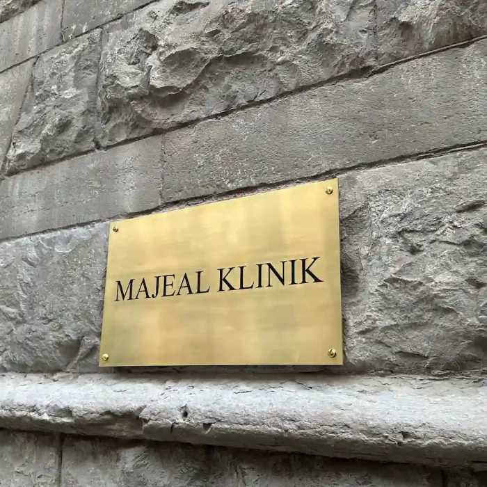 Elegant företagsskylt i mässing för Majeal Klinik, fastsatt på en robust stenfasad i Stockholm. En exklusiv skyltlösning för företag inom vård och hälsa.