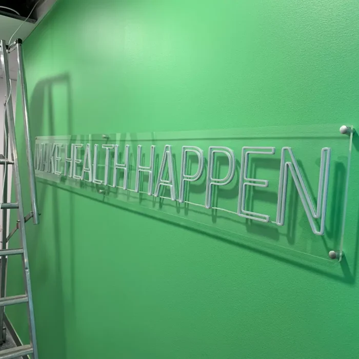Neonskylt Stockholm – Vit neonskylt med texten 'Make Health Happen' på grön bakgrund i Solna.