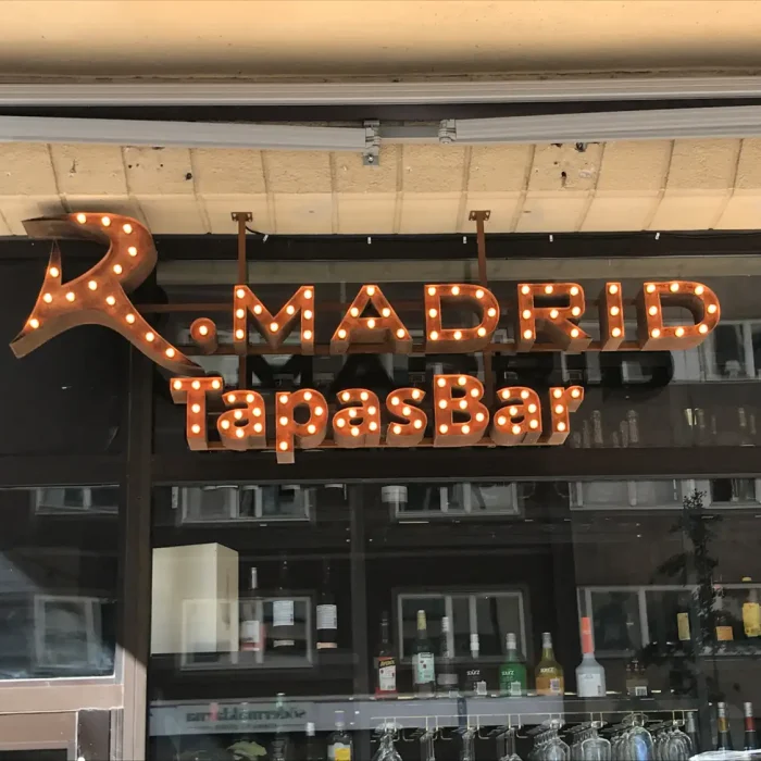 Belyst skylt med en vintage känsla för R. Madrid TapasBar, monterad ovanför en restaurangentré i Stockholm. Ett exempel på dekorativa Företagsskyltar med belysning.