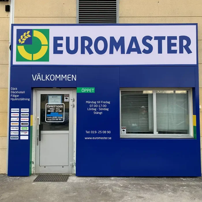 En tydlig och robust plåtskylt vid entrén till Euromaster. Skylten har företagslogotypen och viktig information, monterad på en blå bakgrund för god synlighet.