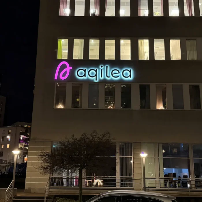 LED skylt för Aqilea, monterad på en kontorsbyggnad i Stockholm med blå och rosa belysning.