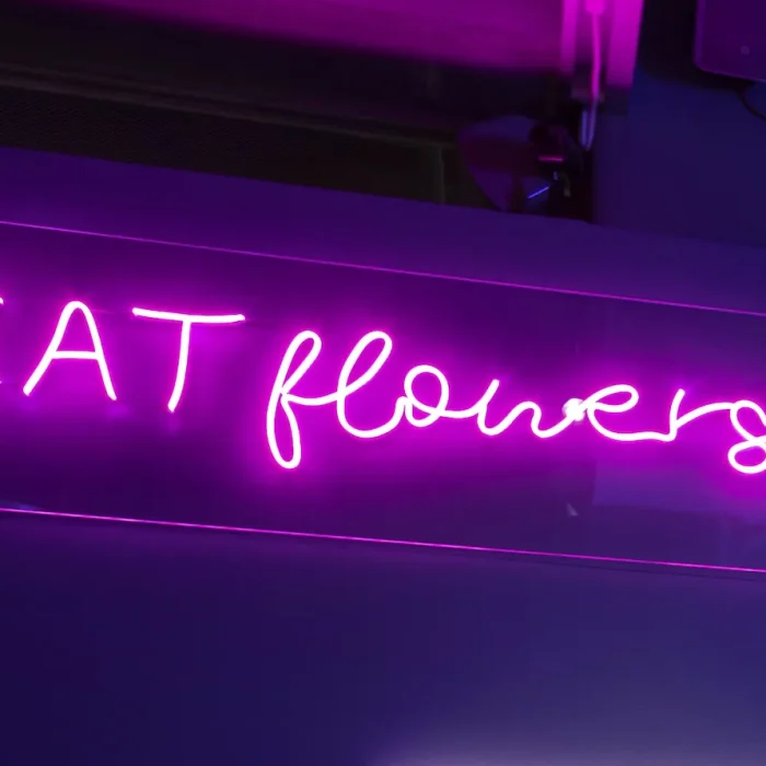 En neoninspirerad lysande skylt med texten "EAT flowers" i rosa. Den genomskinliga bakgrunden gör att skylten smälter in i sin omgivning. Ett kreativt exempel på en lysande skylt med LED och neonstil.