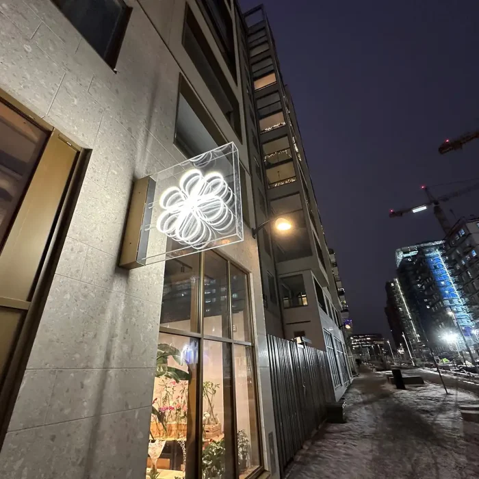En vacker vit lysande skylt i form av en blomma, placerad utomhus vid en butiksentré. Den skapar en modern och exklusiv känsla. Ett exempel på lysande bokstäver och skyltinredning med LED.
