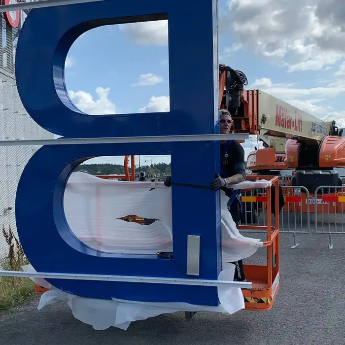 Ett stort blått "B" monteras på en byggnad i Stockholm med hjälp av en skylift.