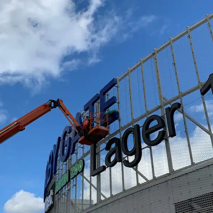 Arbetare monterar en stor fasadskylt på Barkarby Gate i Stockholm med hjälp av en skylift.