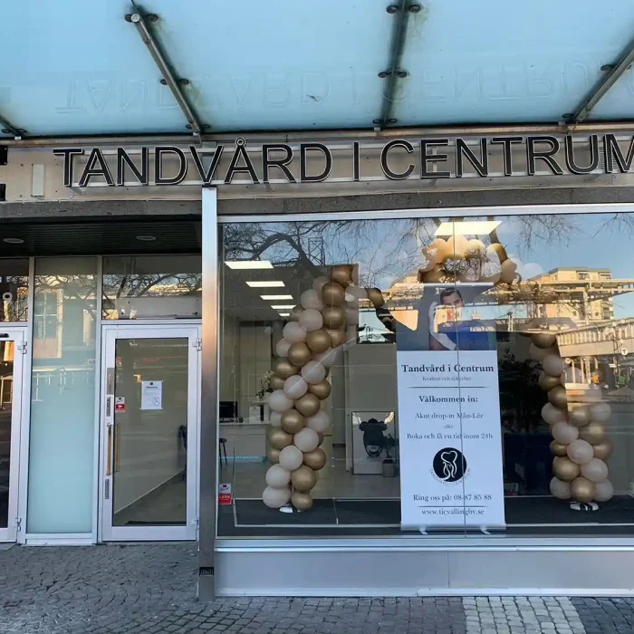Stilren fasadskylt med texten "Tandvård i Centrum" ovanför en glasentré i stadsmiljö – en diskret men professionell skylt fasad som passar för vårdföretag.