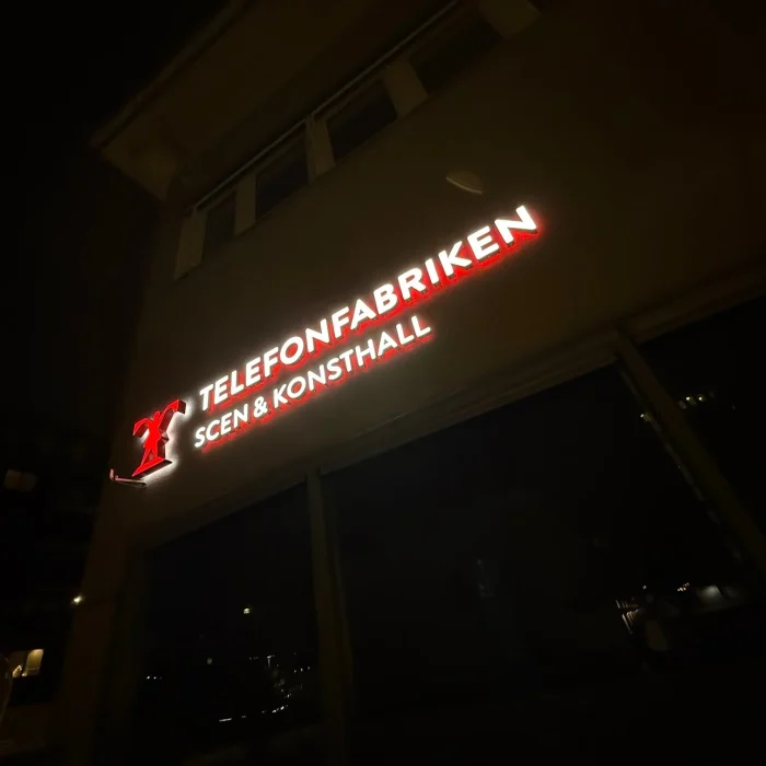 Fasadskylt med röd LED-belysning som lyser upp texten "Telefonfabriken Scen & Konsthall" – ett tydligt exempel på fasadskyltar med LED och stark fasadbelysning skylt för kulturverksamheter.