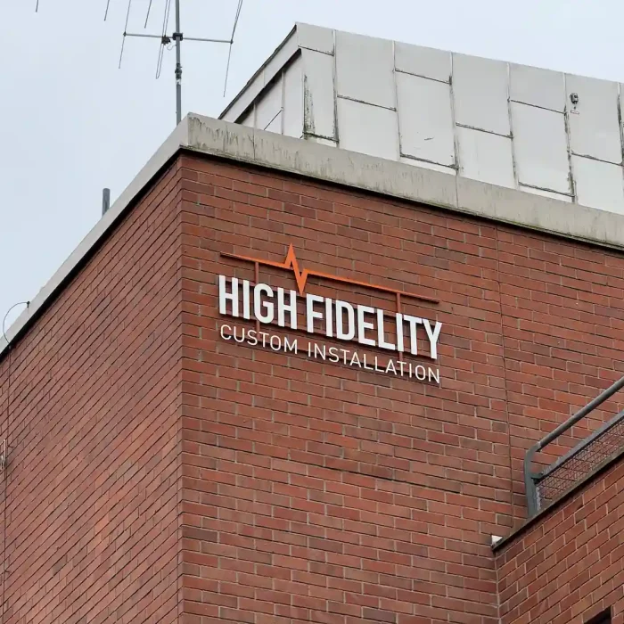 Företagsskylt på tegelvägg för High Fidelity – snyggt monterad företagsskylt utomhus med logotyp.